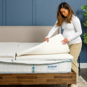Woman unrolling a mattress topper on a bed with a blue wall and plant in the background